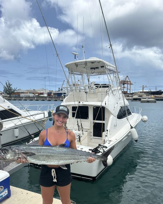 A guest on the dock holding up a wahoo, the boat behind her