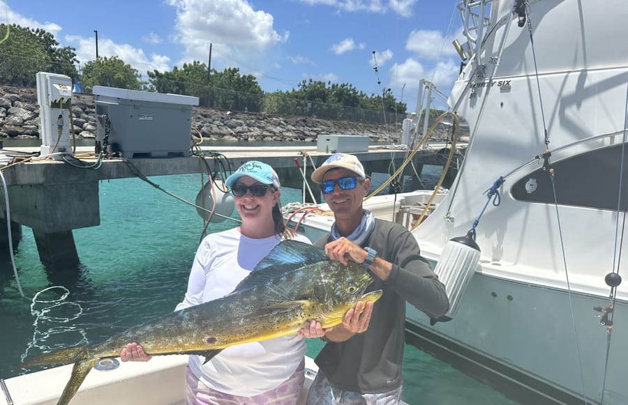 Two guests holding a big mahi mahi on the dock