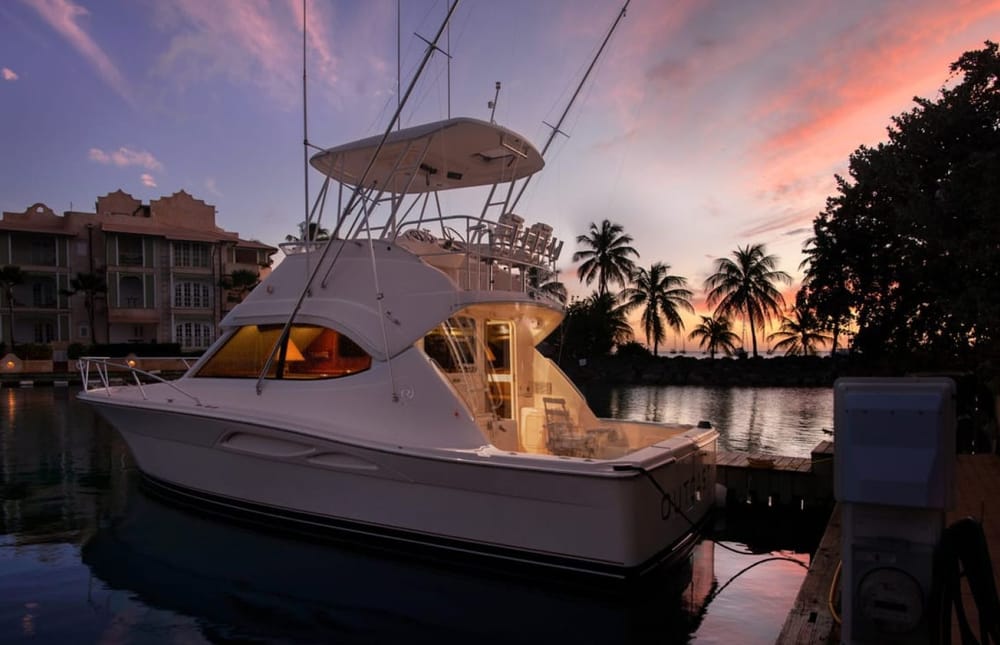 Lucky Penny at her berth at dusk, cabin lights on, palm trees and a pink sky behind