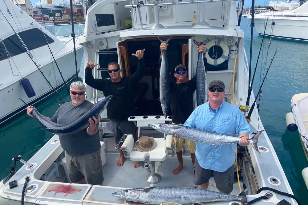 Four anglers in the cockpit holding up wahoo, the boat’s name on the transom