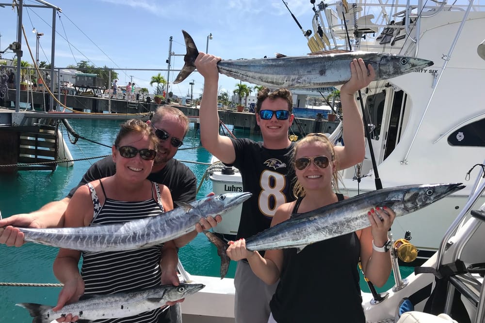 Four guests on the dock holding up wahoo after a trip